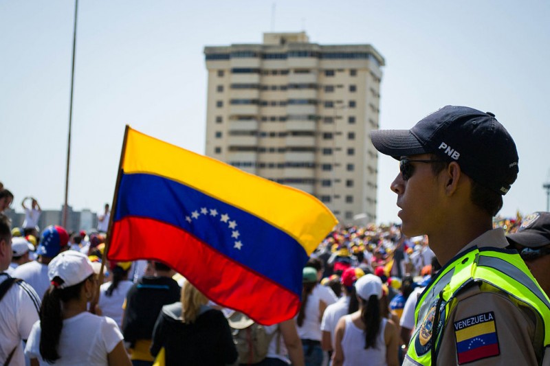 Një oficer i Policisë Kombëtare e të Bolivisë në Venezuelë shikon protestuesit në Maracaibo, 2014. Foto nga Maria Alejandra Mora  (CC BY-SA 3.0)